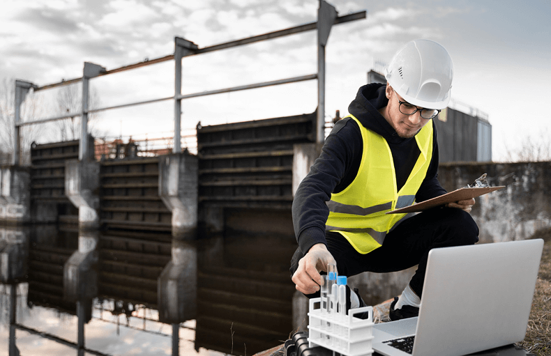 A construction worker in a hard hat and safety vest is engaged with a laptop, emphasizing safety and technology.