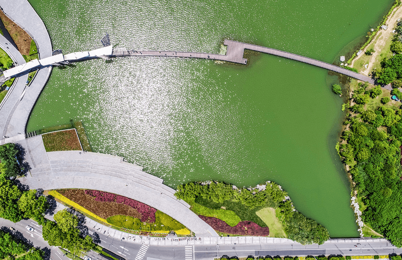 Overhead perspective of a park showcasing a bridge spanning green water, framed by greenery and recreational areas.