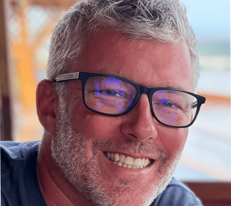 A cheerful man wearing glasses and a beard, showcasing a bright smile that conveys happiness.